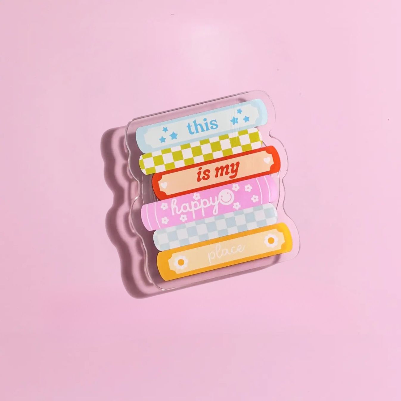 A clear plastic object with colorful bandages and text on it, placed on a pink background.