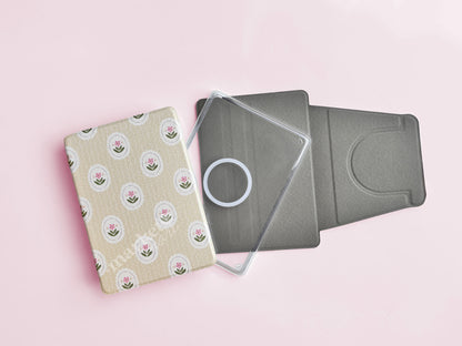 a pink background with a beige book with a floral pattern, a clear plastic case, and a gray case.