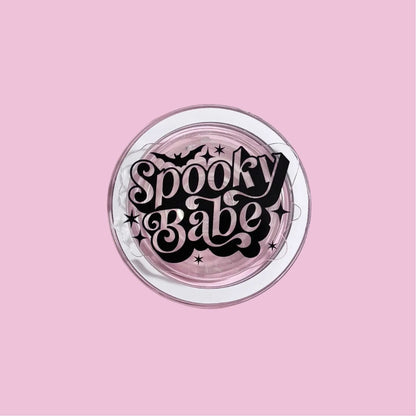 A pink background with a circular design featuring the text "Spooky Babe" in a stylized font.