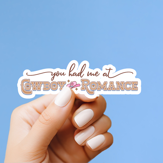 A hand holding a sticker with the text "you had me at Cowboy Romance" against a blue background.
