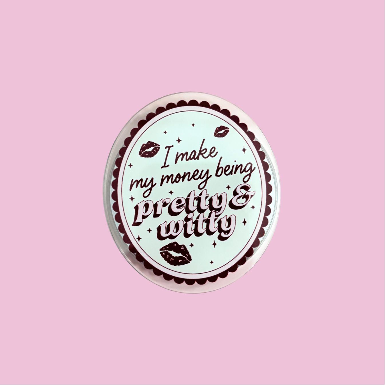 A circular button with the text "I make my money being pretty & witty" printed on it, set against a pink background.