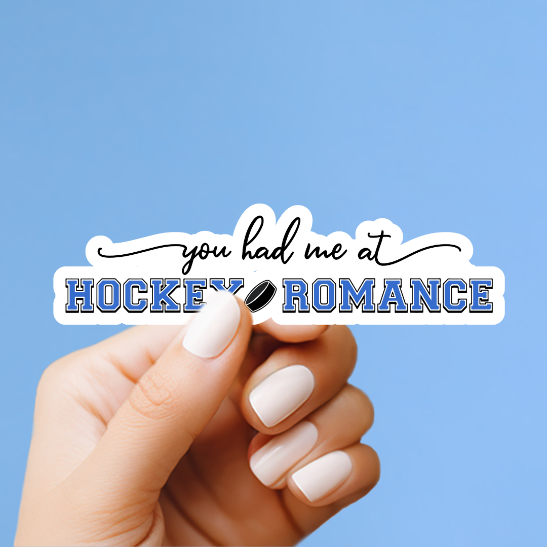 A hand holding a sticker with the text "you had me at HOCKEY ROMANCE" against a blue background.