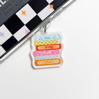 A colorful keychain with the text "this is my happy place" printed on it, hanging on a surface with a checkered pattern.