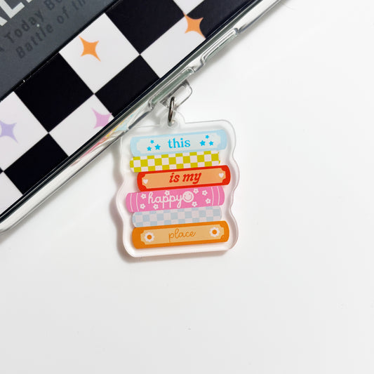 A colorful keychain with the text "this is my happy place" printed on it, hanging on a surface with a checkered pattern.