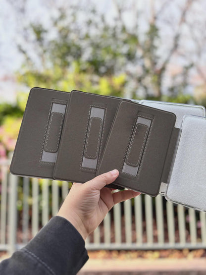 A hand holding a black tablet case with three compartments, against a blurred background of trees and foliage.