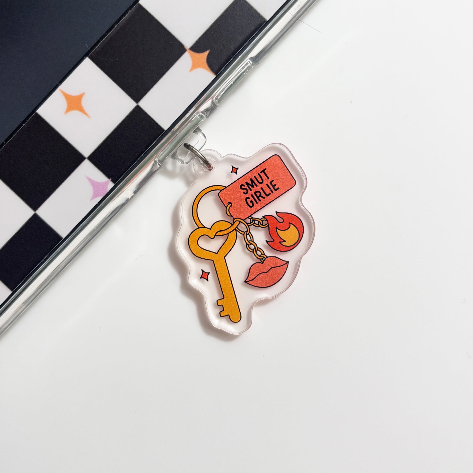a clear plastic charm with a key and a flame design, placed on a white surface next to a black and white checkered pattern.