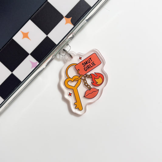a clear plastic charm with a key and a flame design, placed on a white surface next to a black and white checkered pattern.