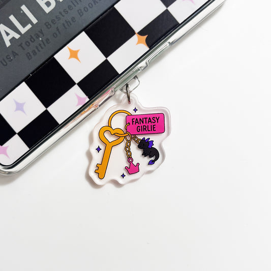 A clear keychain charm with a yellow key and a pink sign that says "FANTASY GIRLIE" is attached to a black and white checkered surface.