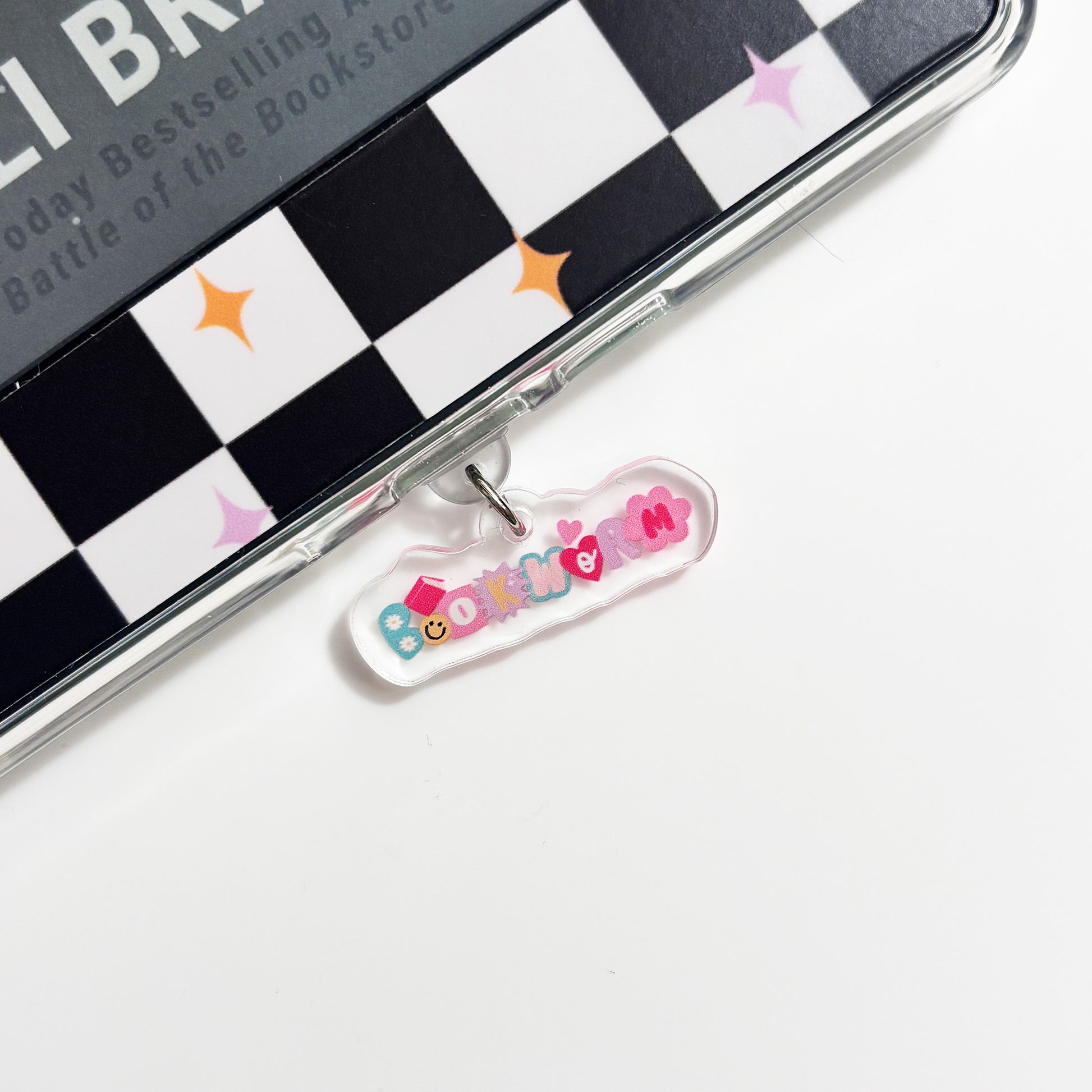 A colorful charm or tag attached to a black and white checkered surface, with the word "Bookworm" written on it.