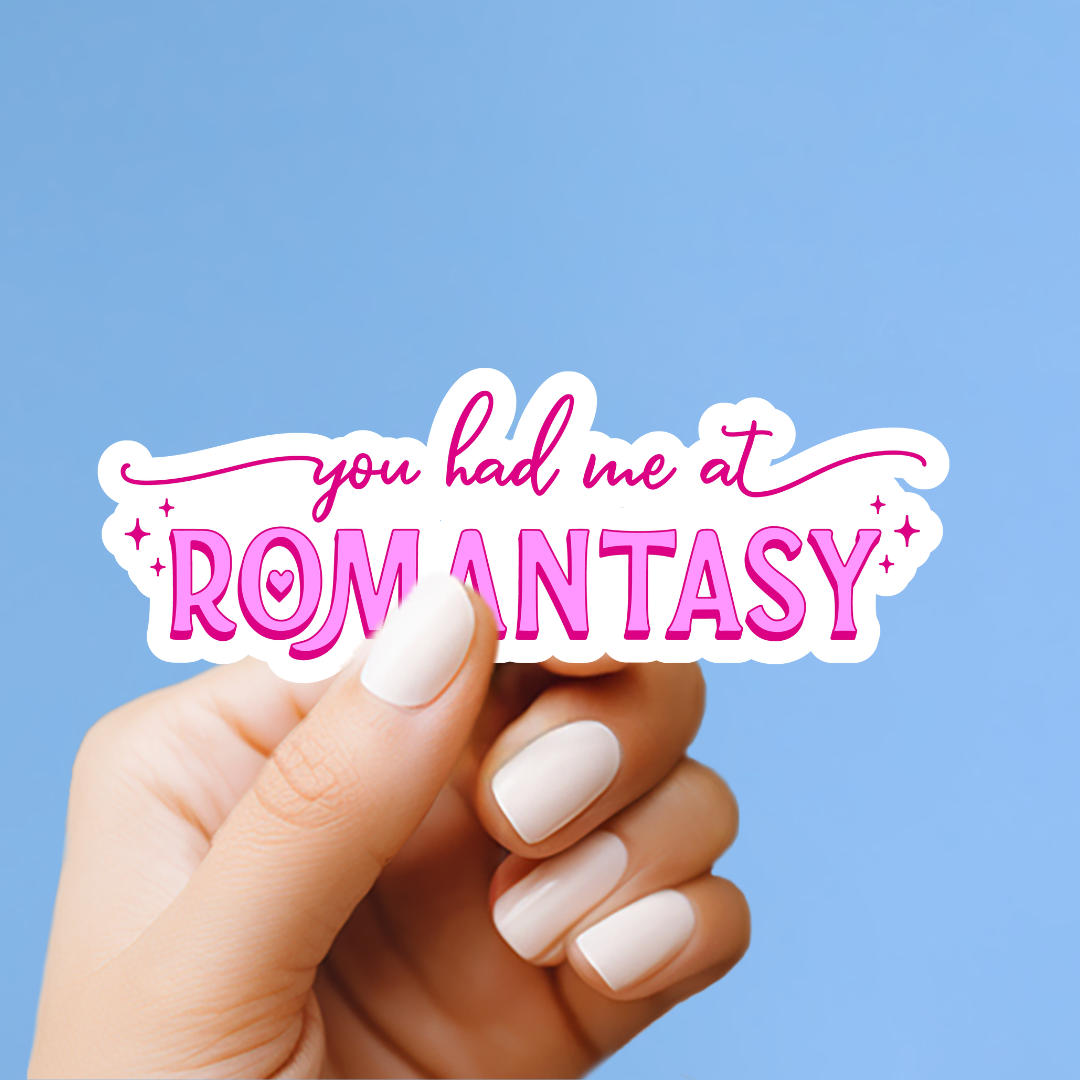 A hand holding a sticker with the text "you had me at ROMANTASY" against a blue background.