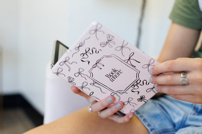 A person is holding a pink book with a bow pattern and the text "Book witch" printed on it.