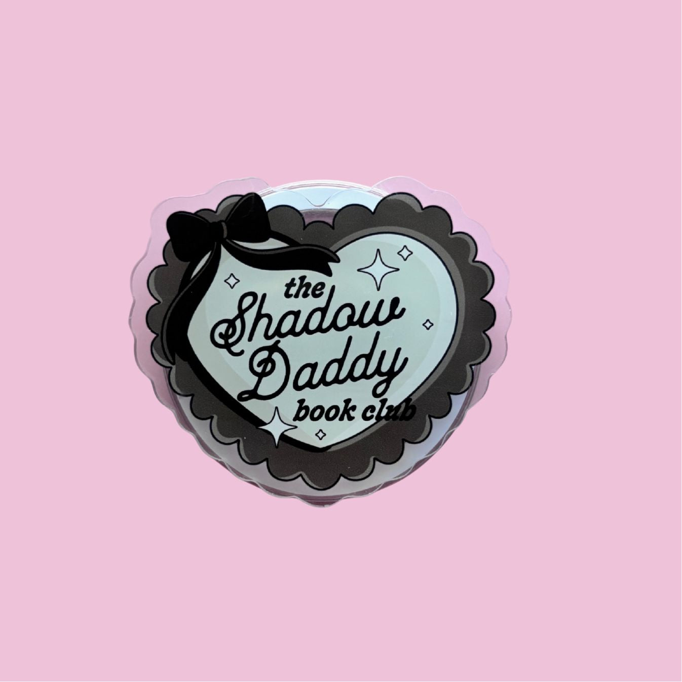 A heart-shaped sticker with the text "the Shadow Daddy book club" on it, set against a pink background.