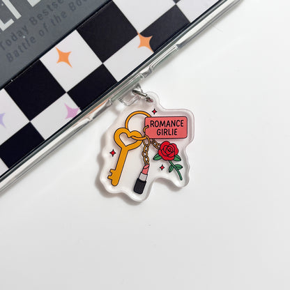 a clear plastic charm with a key and a rose, along with the text "ROMANCE GIRLIE" written on it.