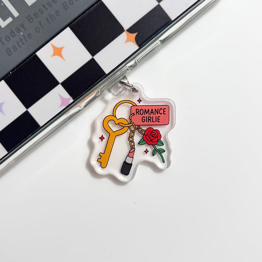 a clear plastic charm with a key and a rose, along with the text "ROMANCE GIRLIE" written on it.