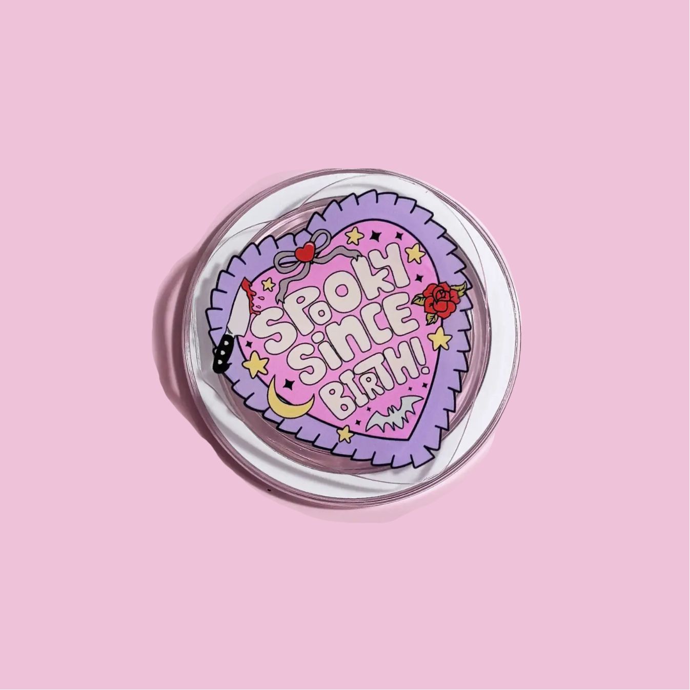 A heart-shaped sticker with a pink background and various decorative elements, including stars, a crescent moon, and a skull.