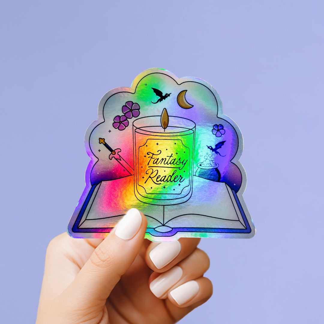A hand holding a colorful sticker with a fantasy reader design, including a candle, flowers, and a book.