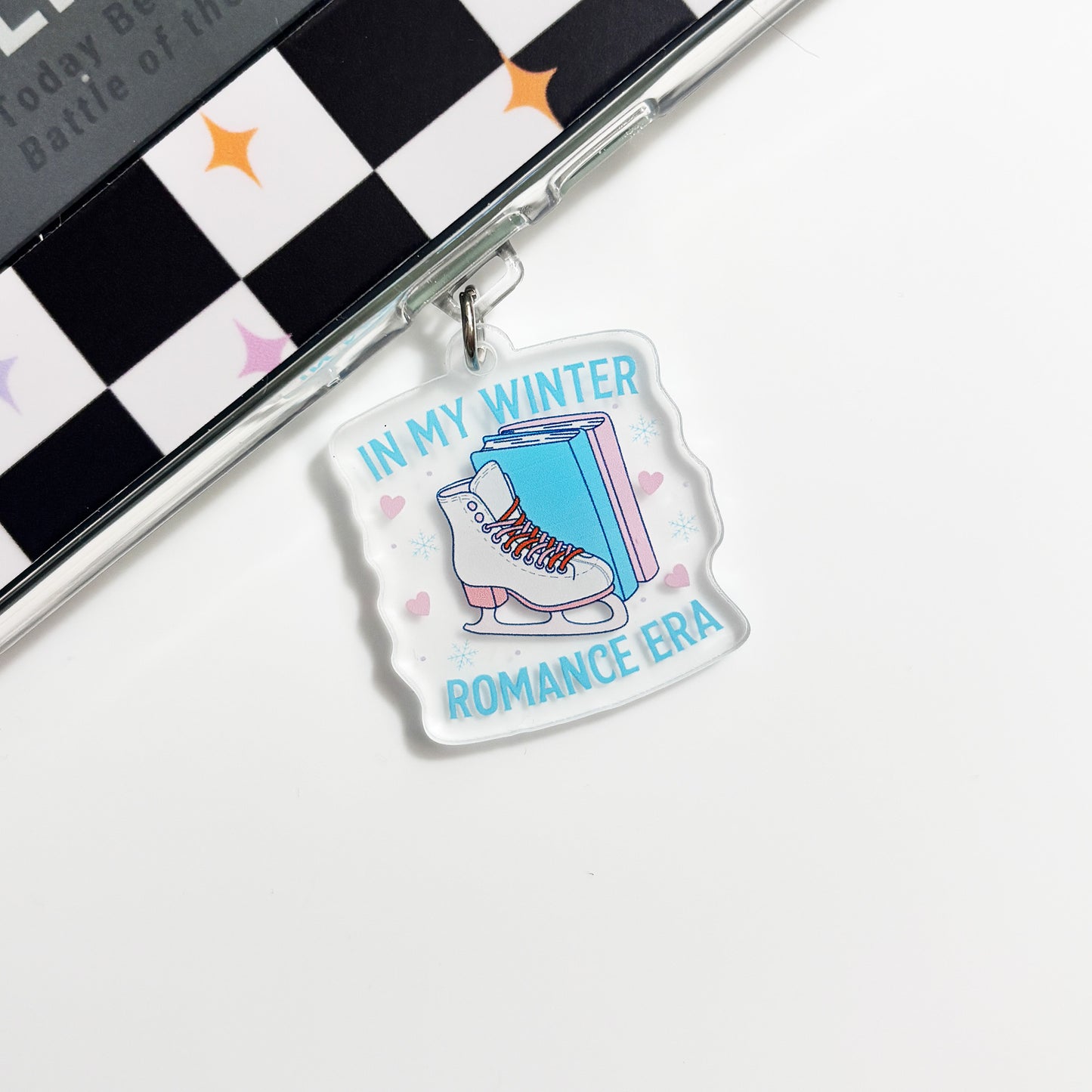 A clear acrylic charm with a graphic design of a pair of skis and the text "IN MY WINTER ROMANCE ERA" printed on it.