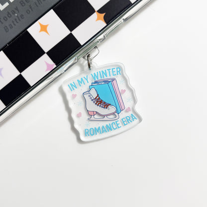 A clear acrylic charm with a graphic design of a pair of skis and the text "IN MY WINTER ROMANCE ERA" printed on it.