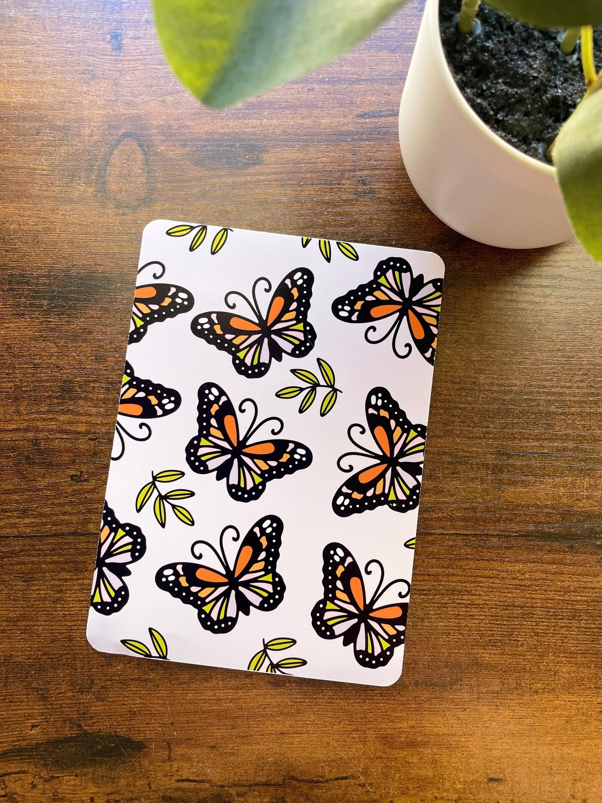 a plant and a butterfly patterned notebook on a wooden table